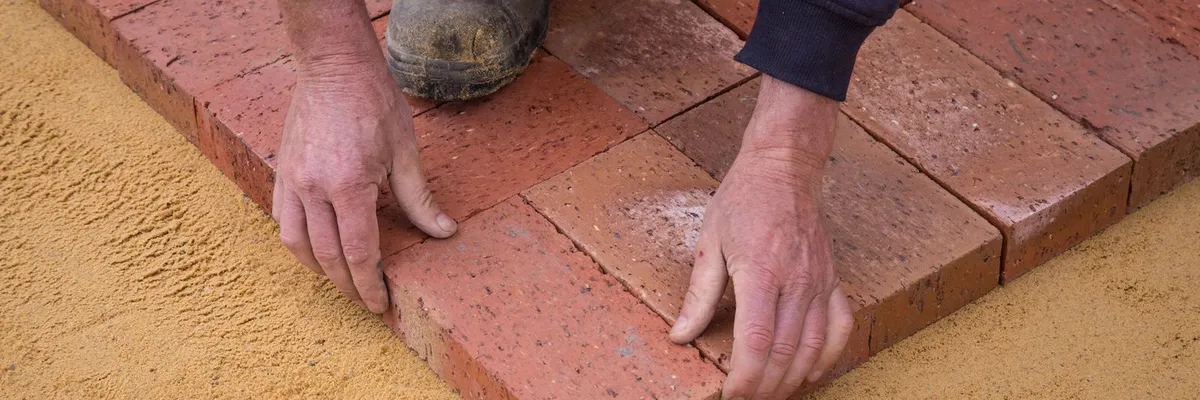 Worker laying patio pavers on a compacted sand base